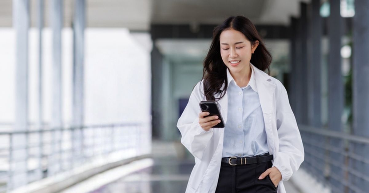 A physician in a white lab coat smiling while looking at her phone