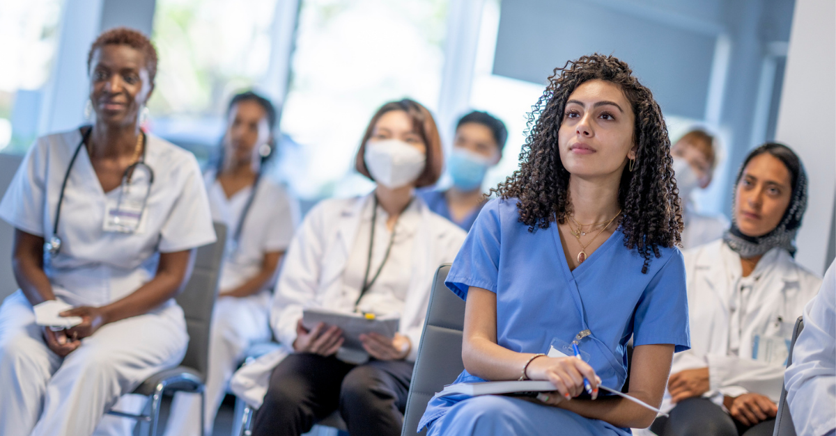 Group of healthcare professionals, including nurses and doctors, seated and attentively listening during a continuing education session