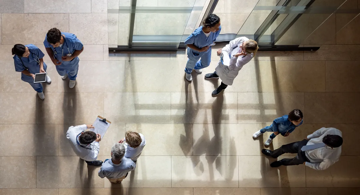 Overhead view of healthcare professionals in scrubs and white coats engaging in a hospital hallway