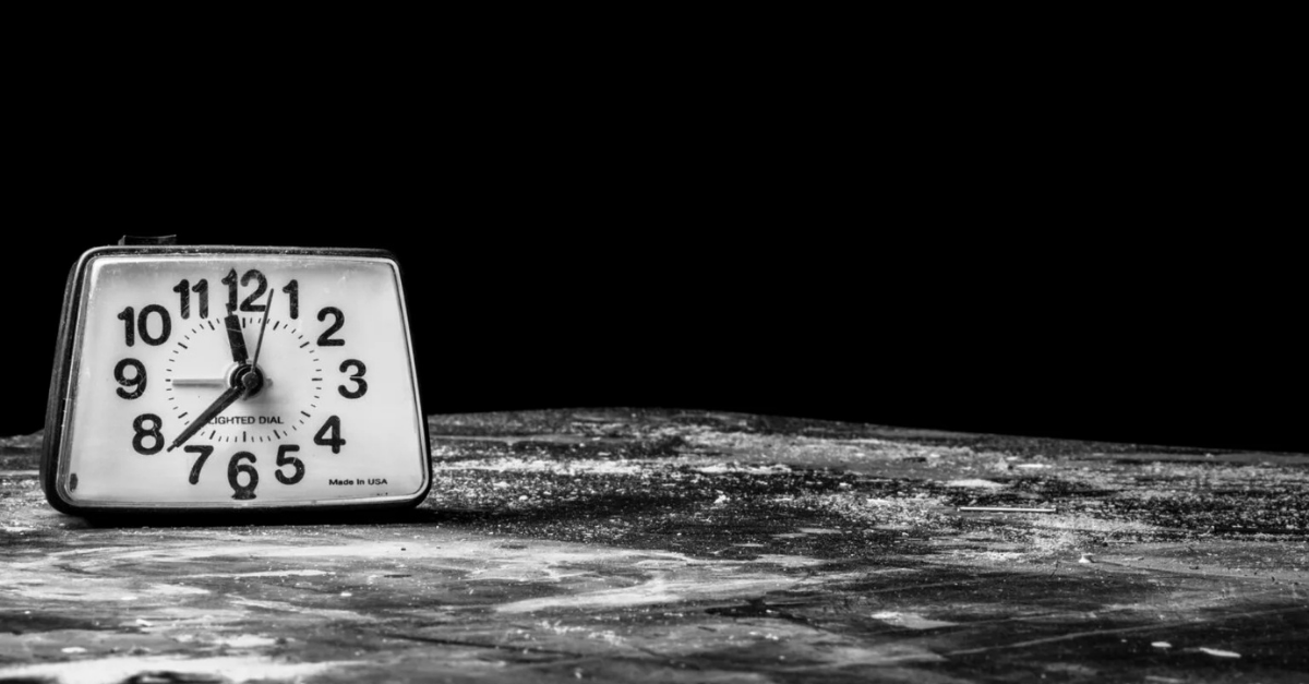 Black-and-white photo of a vintage alarm clock sitting on a weathered surface, symbolizing time and urgency