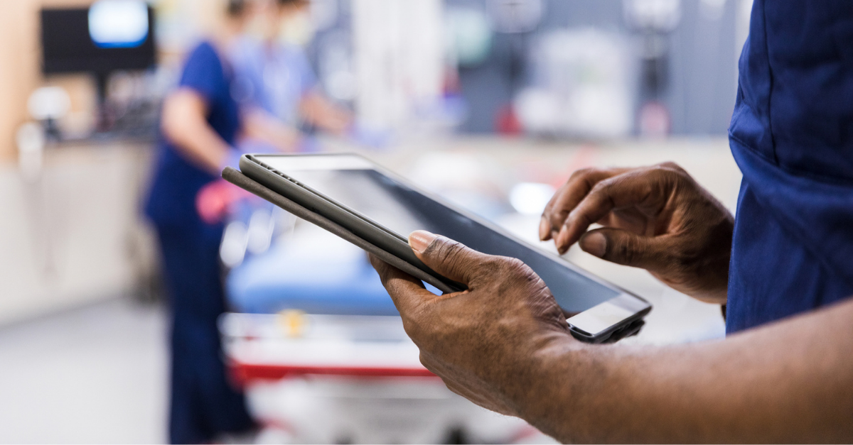 Close-up of a healthcare worker in scrubs holding and using a tablet in a hospital setting.