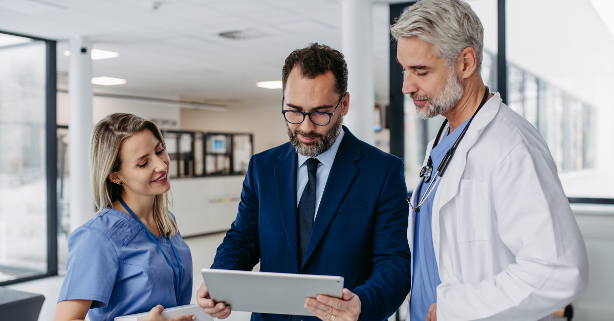 Healthcare administrator and physician in a white coat reviewing information on a tablet with a nurse in scrubs.