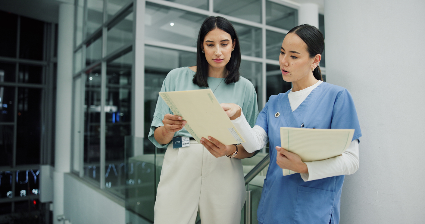 Two female healthcare professionals reviewing patient documents together in a hospital hallway
